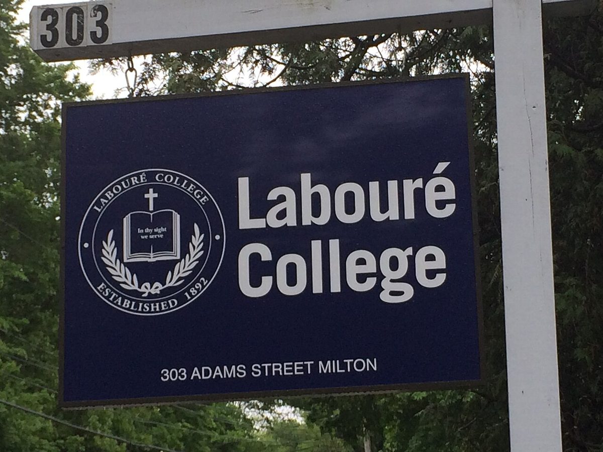 Navy sign reading Labouré College, 303 Adams Street Milton, hanging from a white post